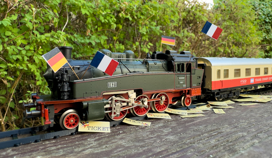 A model of a steam locomotive with French and German flags,a Trans-Europ-Express wagon attached. The train is losing tickets