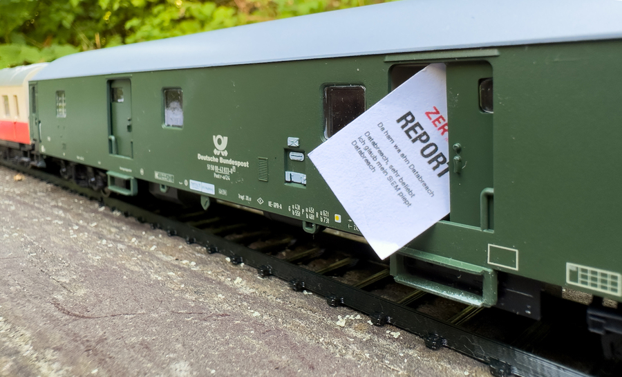 The model train's mail car, in the open door an oversized paper with the inscription ZER-Report